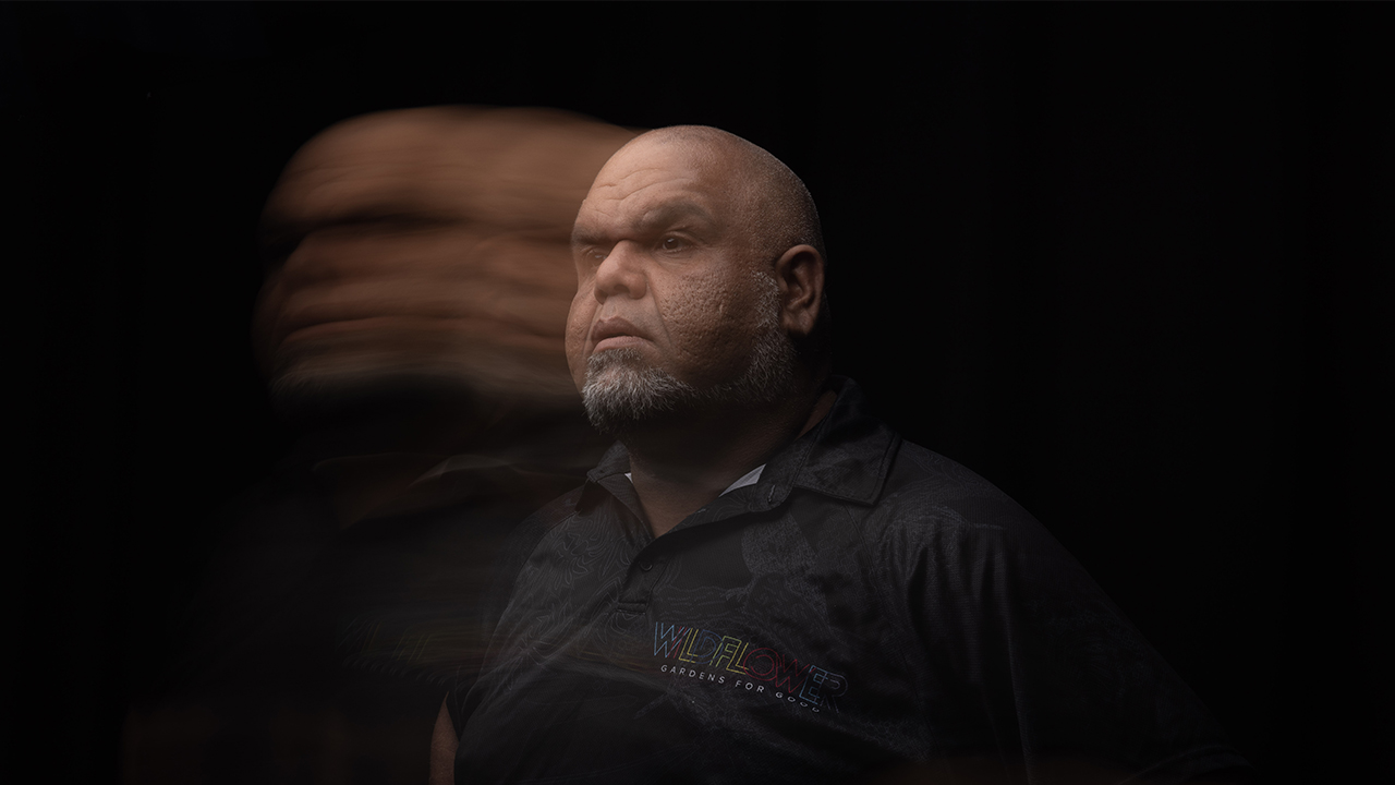 Man with blurred face effect standing in front of a black background.