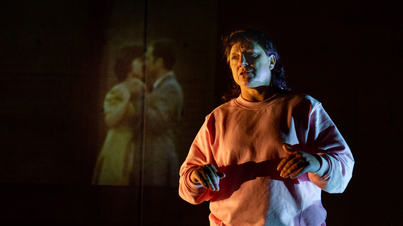 Kaz Therese stands in front of a projection of a couple dancing.