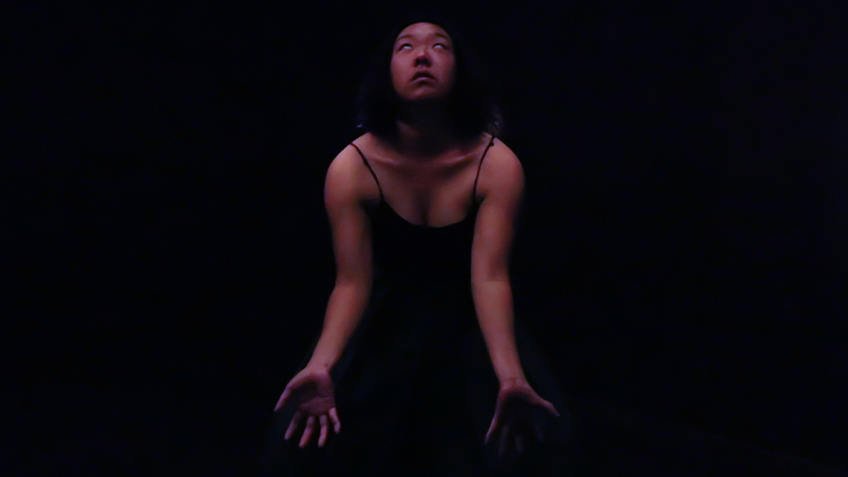 A person dressed in black looks up with their palms facing outward.