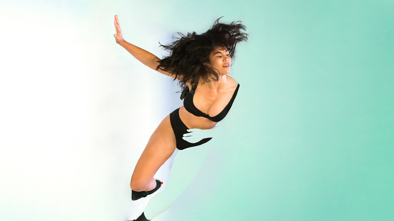 Amrita Hepi leans against a white/ green background.