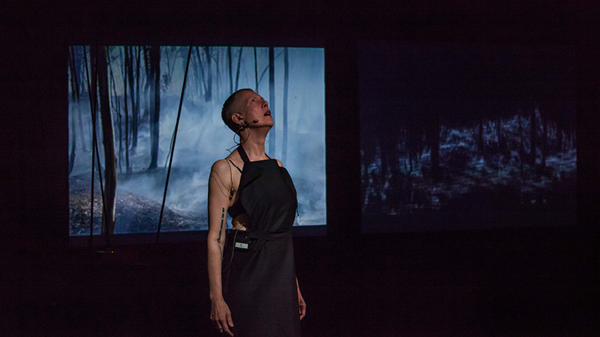 BoneDirt stands looking upwards with two screens behind them.