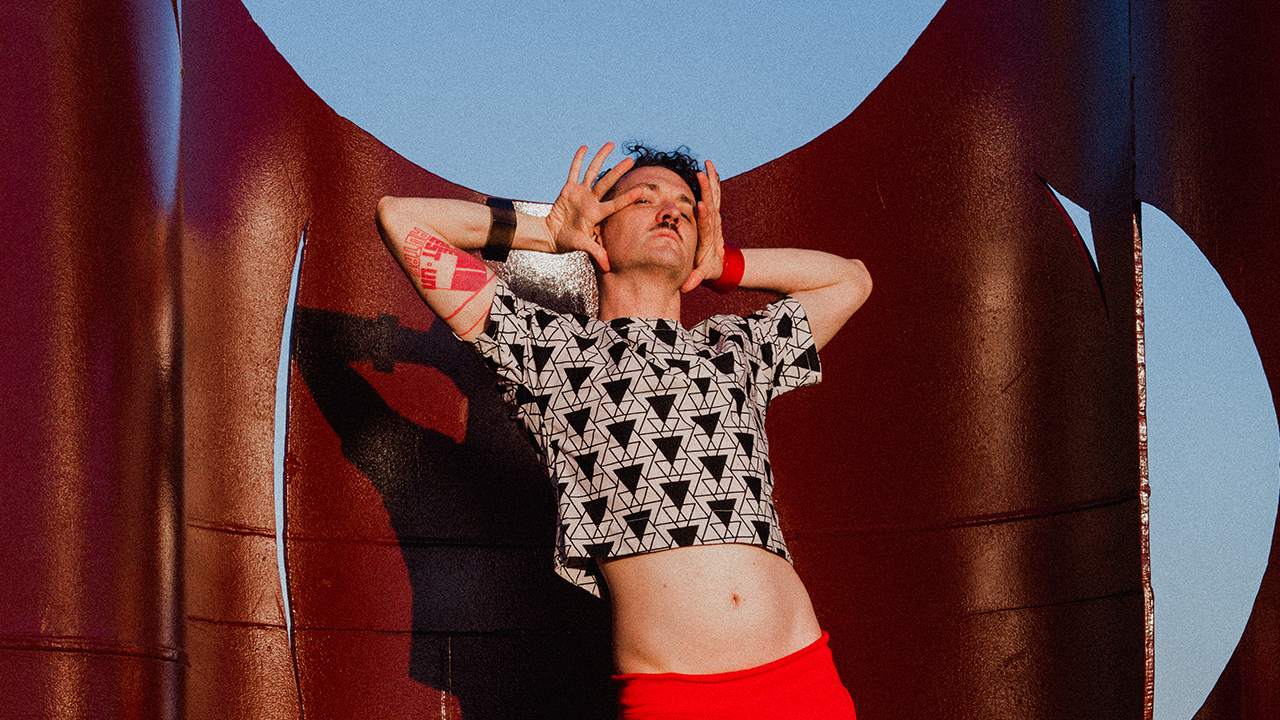 person with red pants and black and white shirt lean backwards with hands up to their face